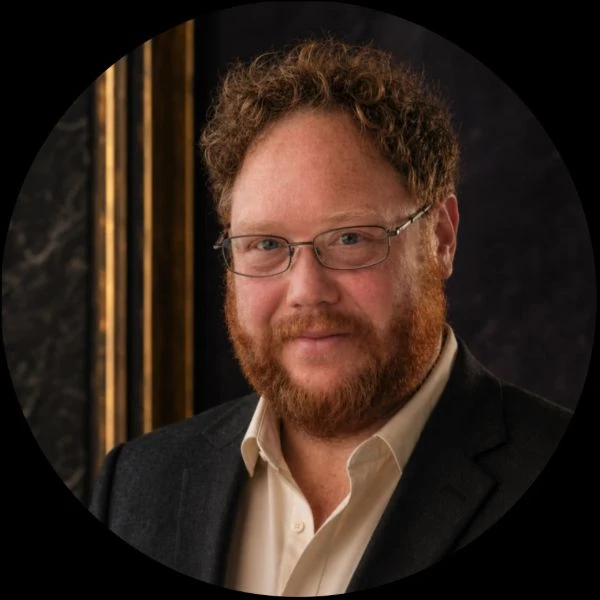 Byron Lee, wearing glasses and a dark blazer